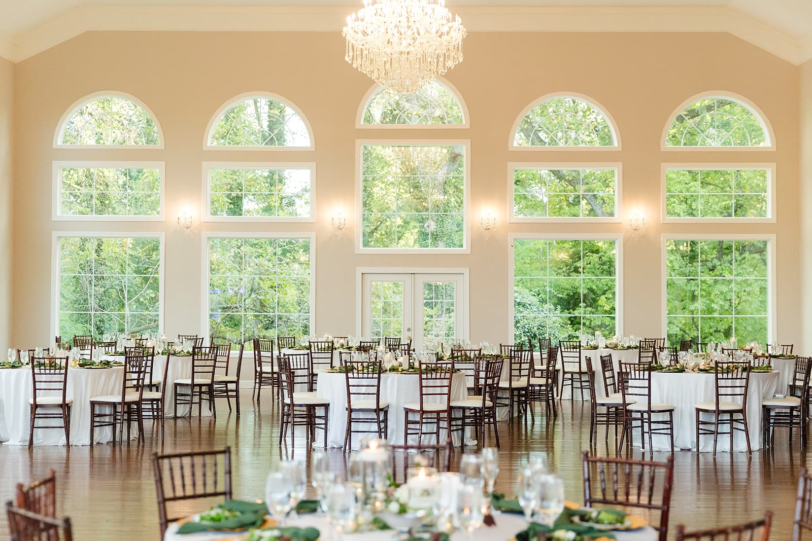 Glass-walled ballroom with arched windows and a chandelier set for dinner